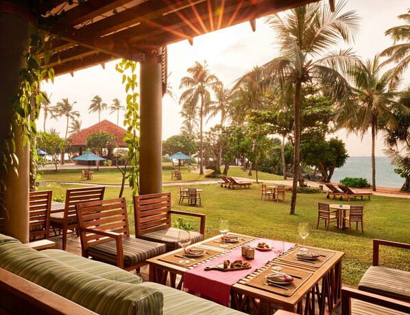 A tropical outdoor dining area with wooden furniture and a view of the ocean.