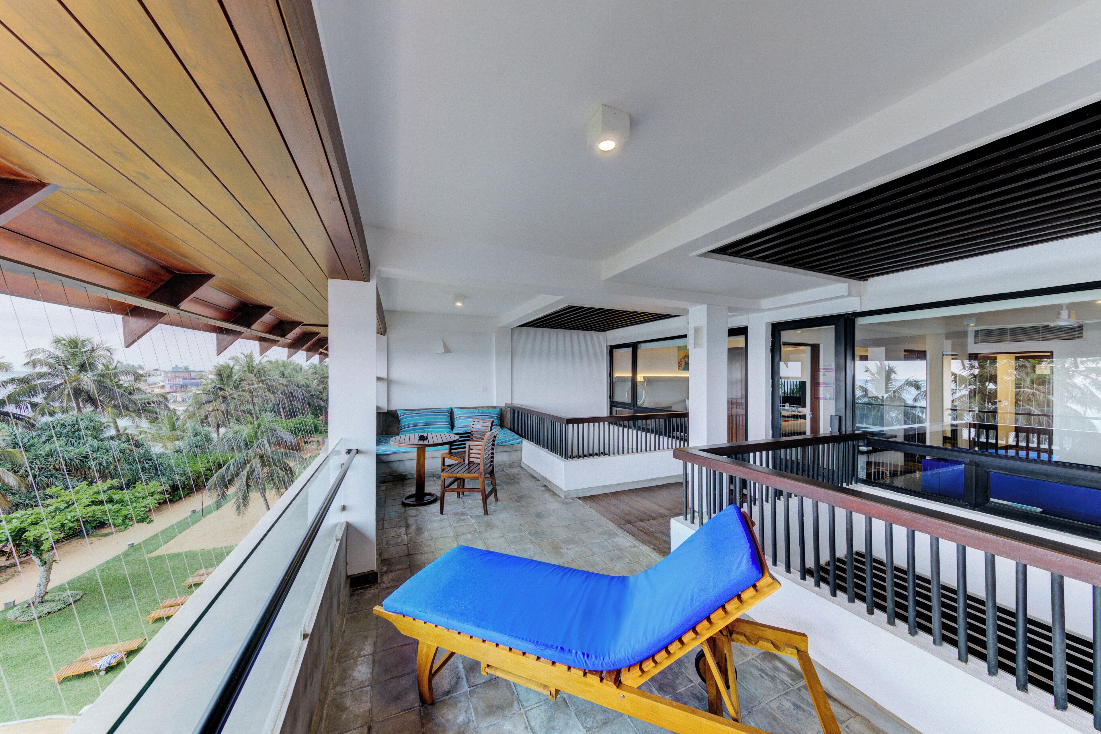 A balcony with a blue cushioned lounge chair, a wooden table, and a seating area with striped cushions.