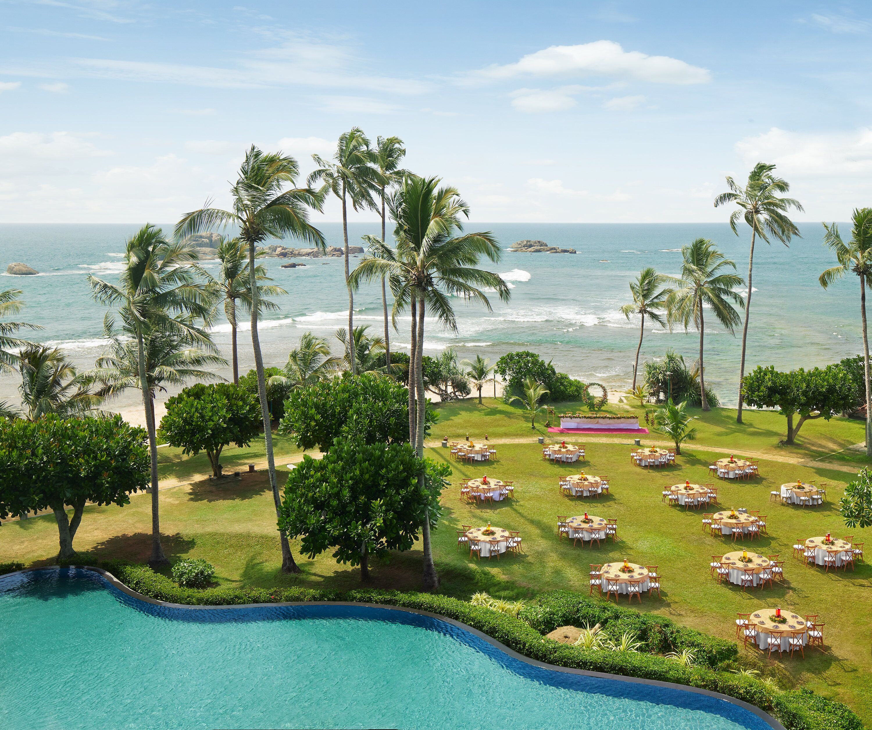 A poolside view with a beachfront setting, palm trees, and outdoor dining areas.