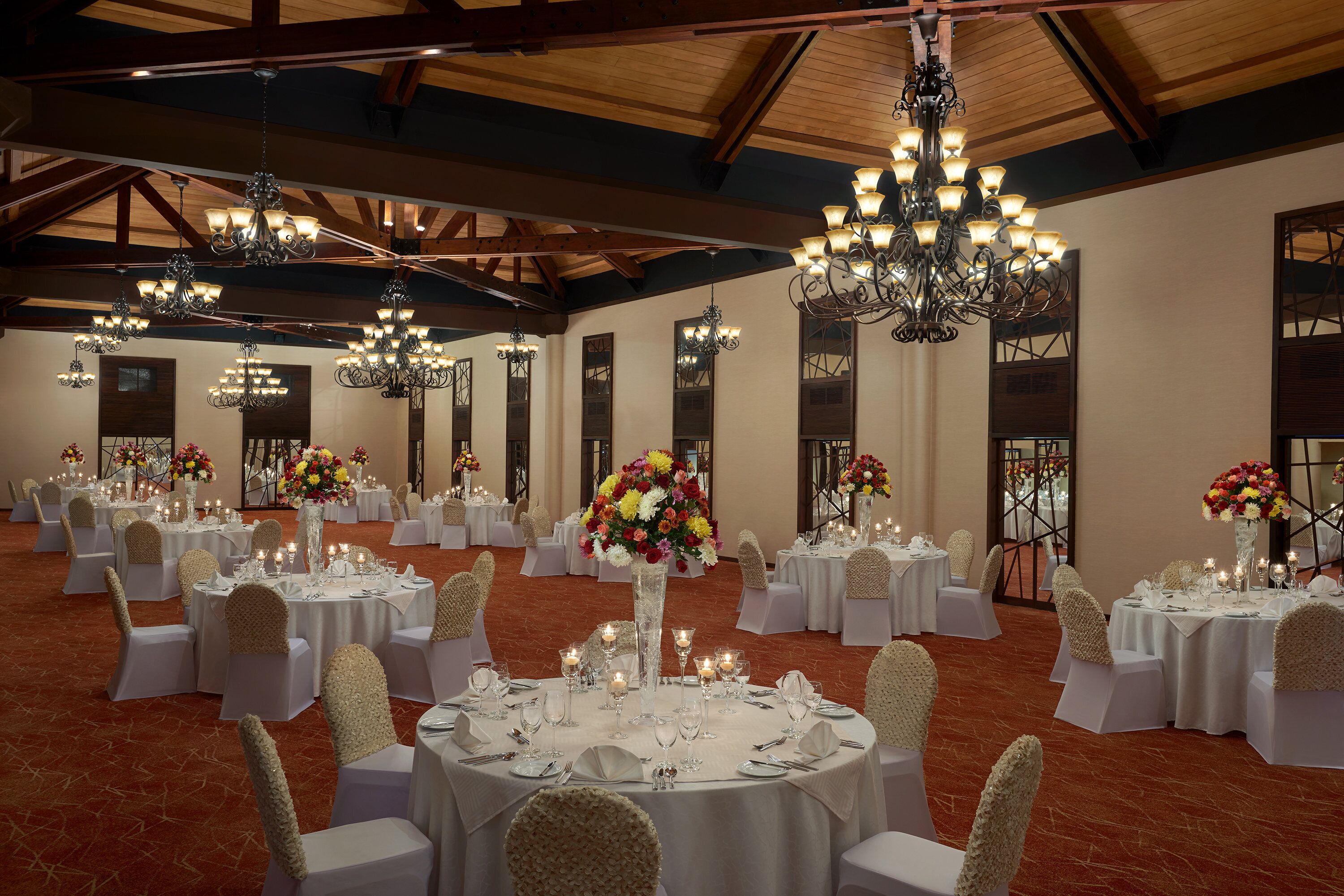 A banquet hall with round tables set for events, chandeliers, and floral centerpieces.