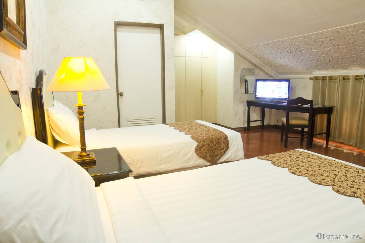 Habitación de hotel con dos camas, un escritorio con computadora y una lámpara.