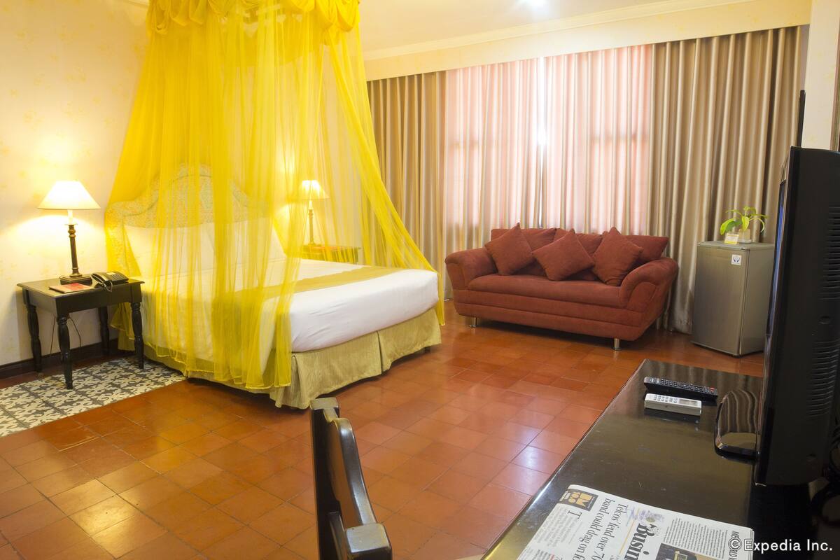 Una habitación de hotel con una cama, un sofá, un televisor y un escritorio con lámpara.