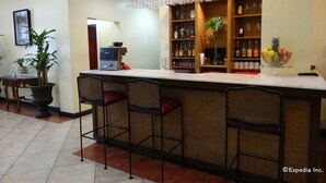A bar area with a coffee machine, bar stools, a fruit bowl, and shelves with bottles and glasses. - White Knight Hotel Intramuros (Manila)