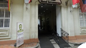 The entrance to the White Knight Hotel Intramuros with a sign above the door, a staircase leading up, and a banner on the wall. - White Knight Hotel Intramuros (Manila)