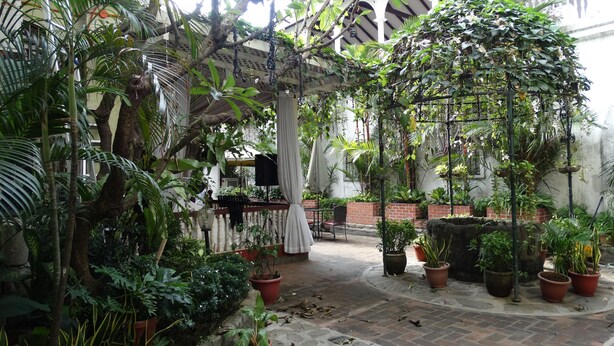 A lush indoor garden with potted plants, a stone floor, and a white gazebo. - White Knight Hotel Intramuros (Manila)