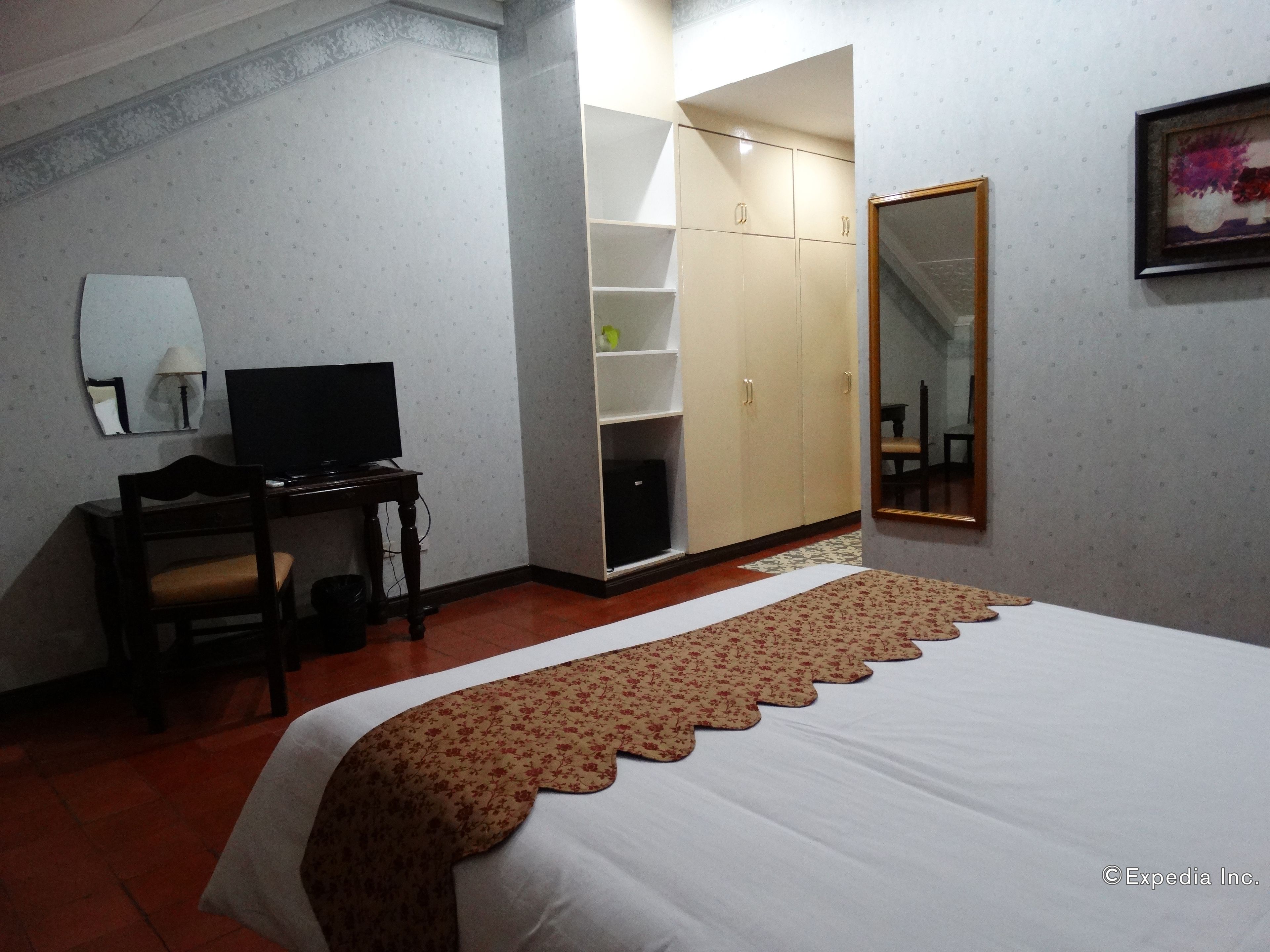 Une chambre d’hôtel comprenant un lit, un bureau avec une télévision, une armoire et un miroir.