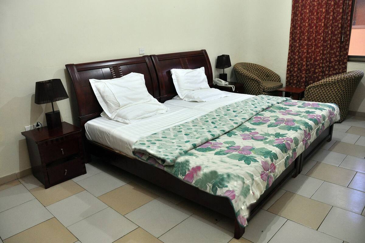 A neatly made bed with a floral bedspread, two bedside tables with lamps, and a chair in a corner.