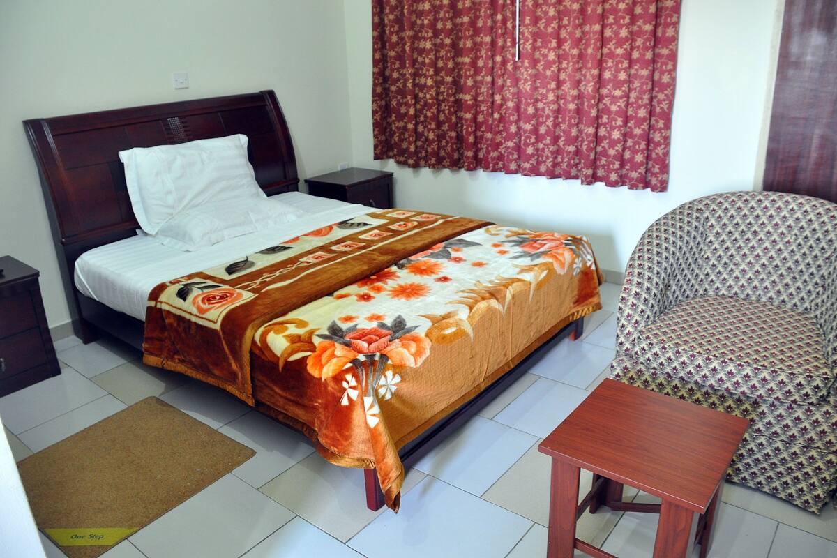 A bedroom with a bed, a bedside table, a chair, and a small wooden table.