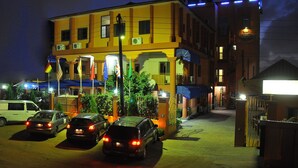 Un hotel de varios pisos con fachada amarilla, múltiples banderas y una entrada protegida por una reja.