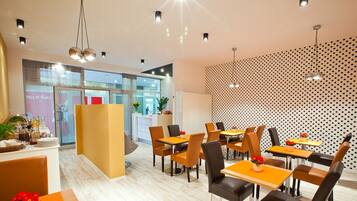 A modern dining area with multiple tables and chairs, a reception desk, and a patterned wall.