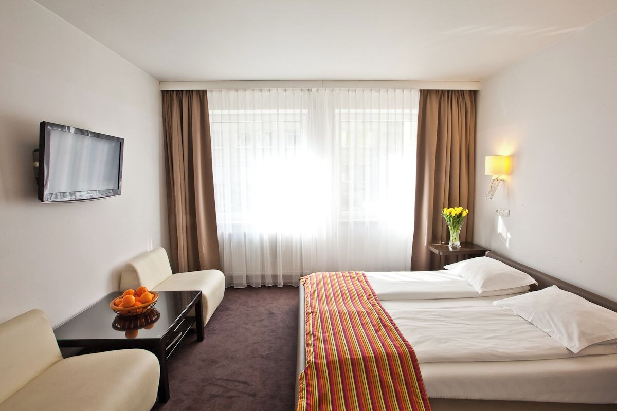 A hotel room with two beds, a TV, a desk with a bowl of fruit, and a vase with flowers.