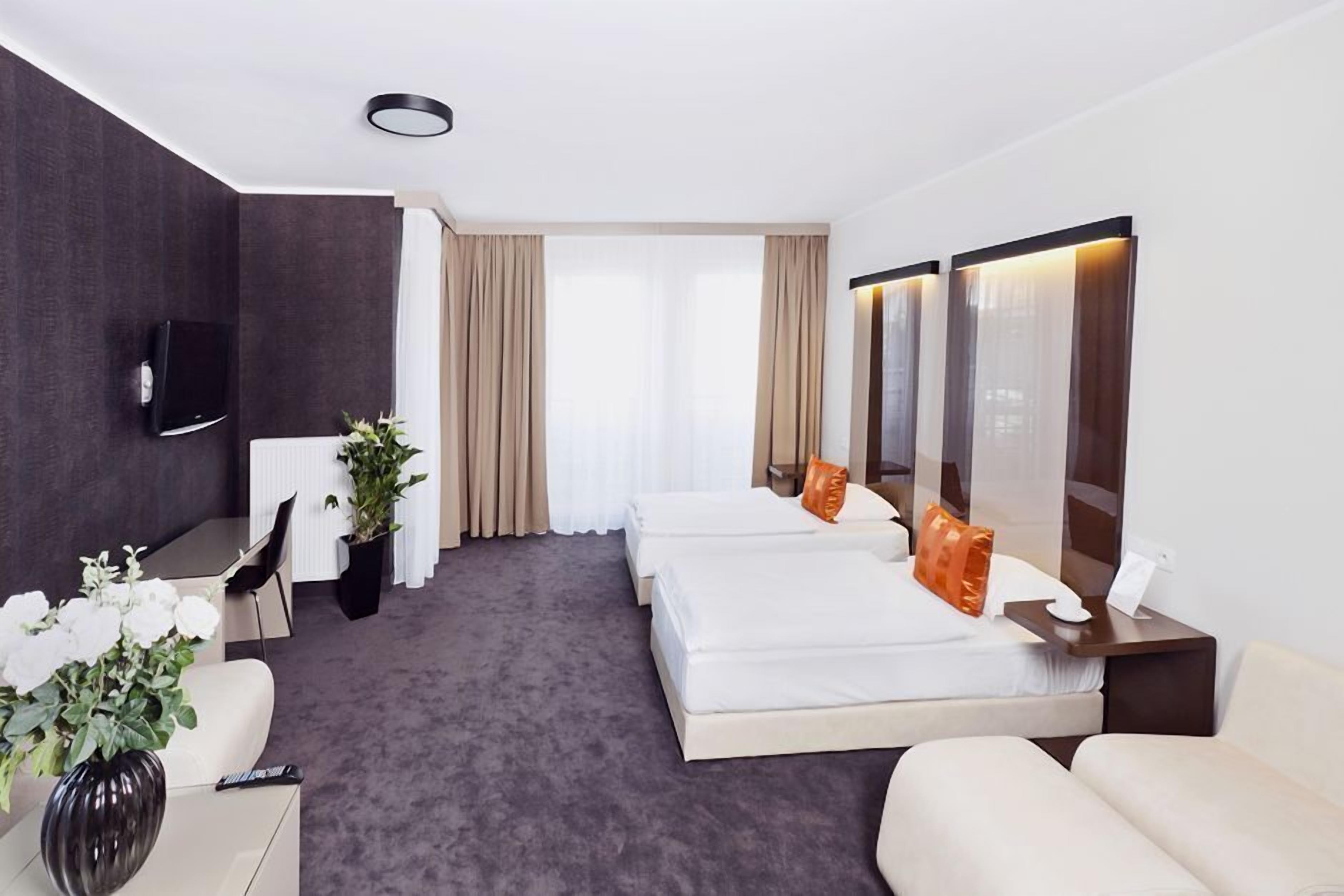 Hotellihuone, jossa on sänky, työpöytä, tuoli, televisio ja suuri ikkuna, jossa on verhot.
