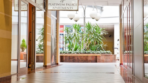A modern hotel lobby with a sign for Platinum Palace Apartments, a reception desk, and a plant area. - Platinum Apartments Aparthotel (Poznan)