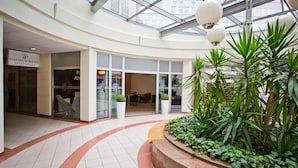 A modern atrium with a glass ceiling, featuring a Platinum Palace sign, a central planter with greenery, and a curved walkway. - Platinum Apartments Aparthotel (Poznan)