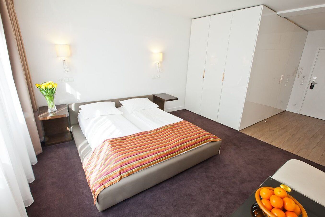 Una habitación de hotel con cama, mesitas de noche, armario y una pequeña mesa con un florero.