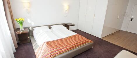 Una habitación de hotel con cama, mesitas de noche, armario y una pequeña mesa con un florero.
