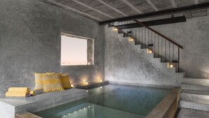 Une piscine intérieure moderne avec un revêtement intérieur en béton, un escalier avec des rampes en bois et une fenêtre offrant une vue.