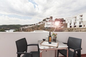 A terrace with a table set for two, a bottle of wine, and glasses. A view of a white building with a tower is visible in the background.