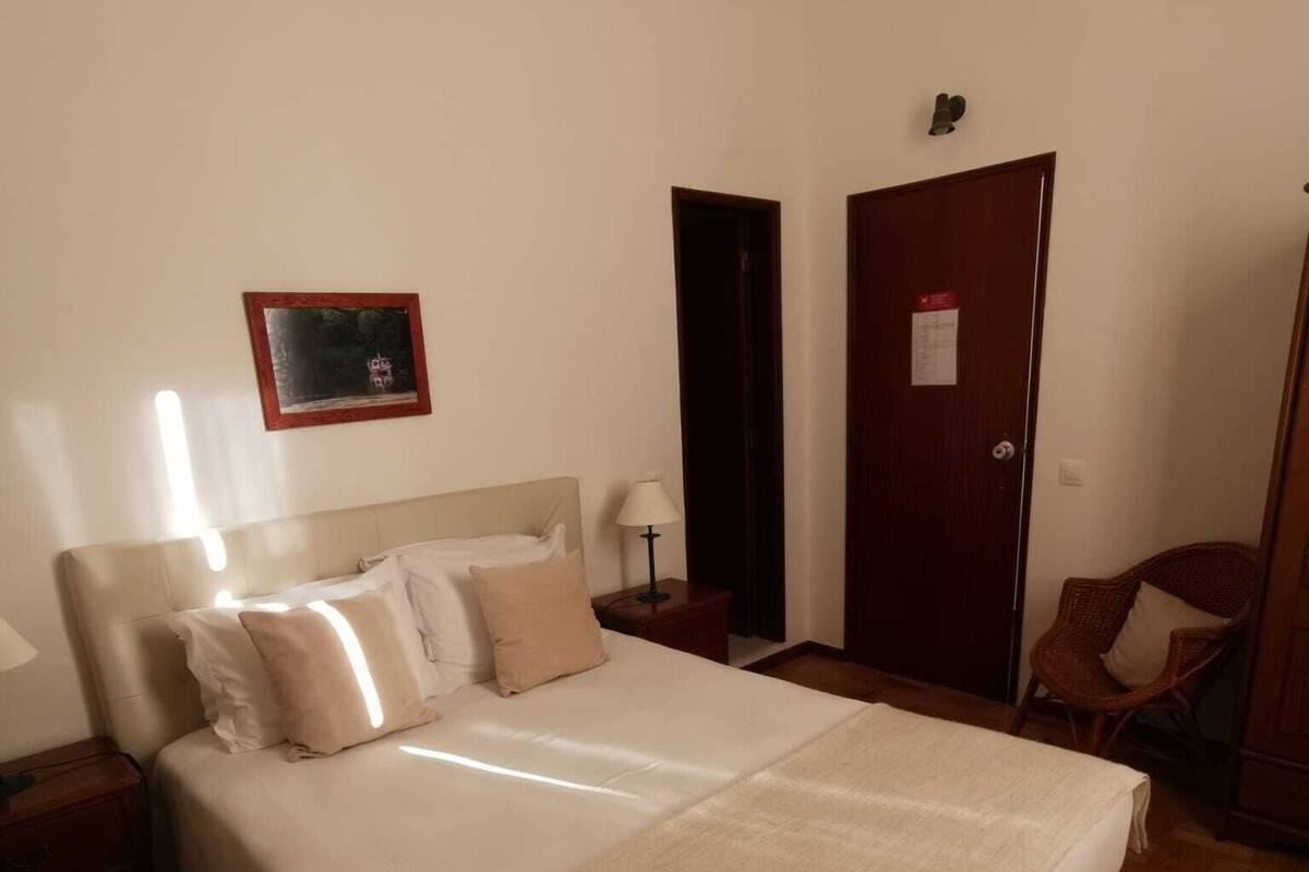 A bedroom with a large bed, a nightstand, a chair, a door, and a framed picture on the wall.