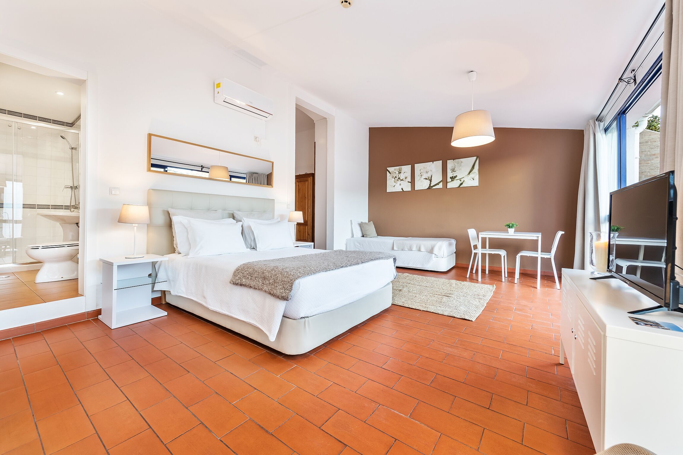 A modern bedroom with a large bed, bedside tables, a desk, and a TV.