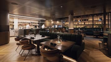 Un interior de restaurante con zona de bar, mesas y sillas, y una cocina al fondo.