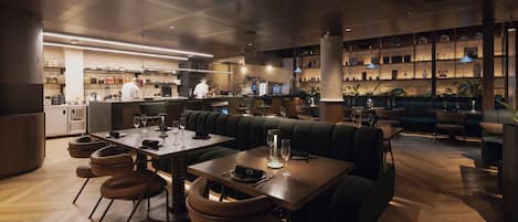 A restaurant interior with a bar area, seating arrangements, and a kitchen in the background.