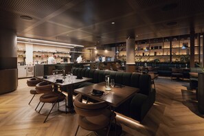 Un interior de restaurante con zona de bar, mesas y sillas, y una cocina al fondo.