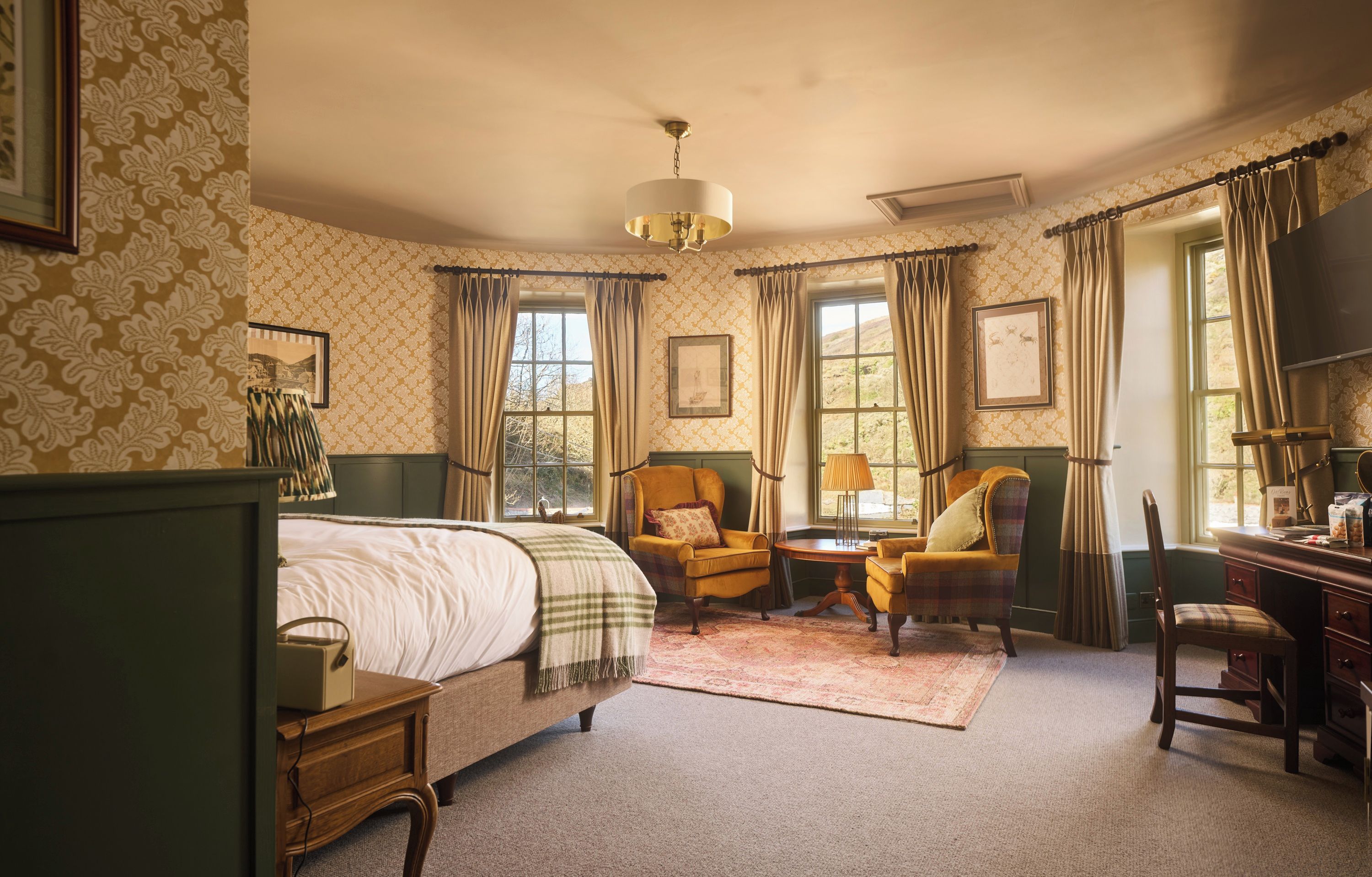 A traditional bedroom with a bed, two armchairs, a desk, and a window with curtains.