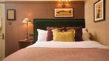 Une chambre d’hôtel avec un grand lit, une tête de lit recouverte d’un tissu vert, une lampe fixée au mur et des œuvres d’art encadrées.