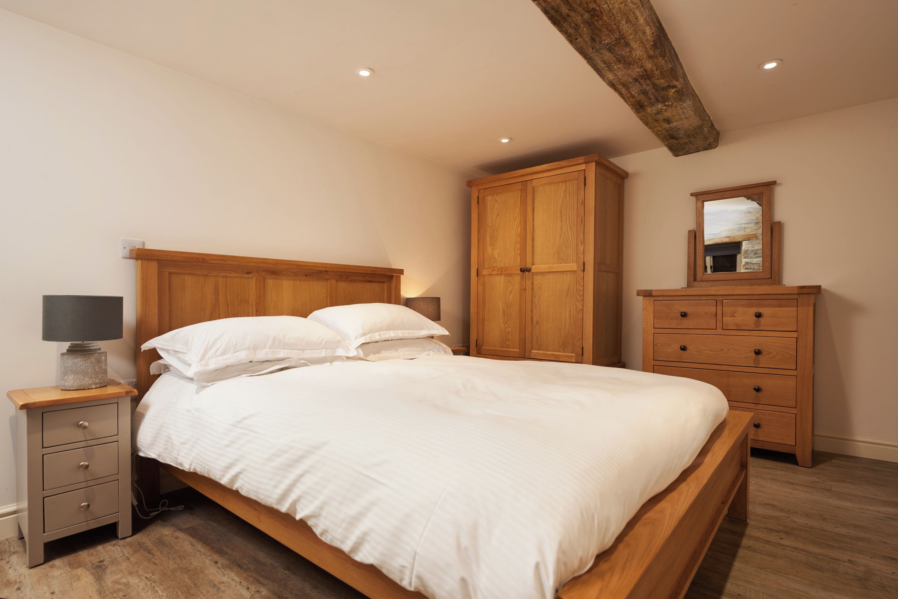 A bedroom with a wooden bed, a nightstand with a lamp, a wardrobe, and a mirror on the wall.