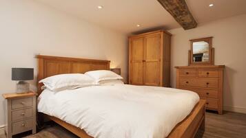 A bedroom with a wooden bed, a nightstand with a lamp, a wardrobe, and a mirror on the wall.