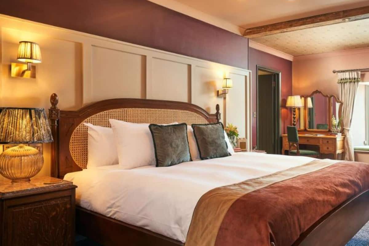 A neatly made bed with a wooden headboard, a nightstand with a lamp, and a dresser with a mirror.