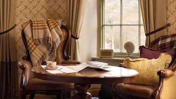 A room with a round wooden table, two chairs, a sofa, and a window with curtains.