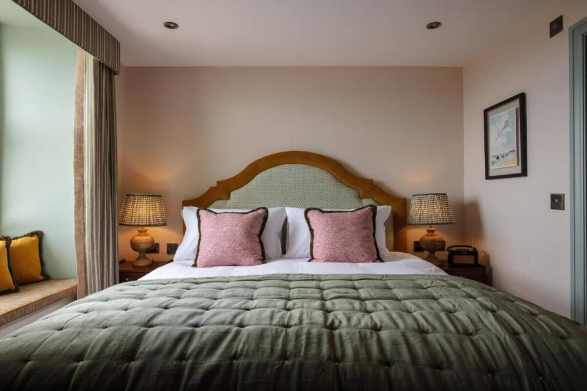 A neatly made bed with a green quilt, two pink pillows, and a wooden headboard. There are two bedside lamps and a framed picture on the wall.