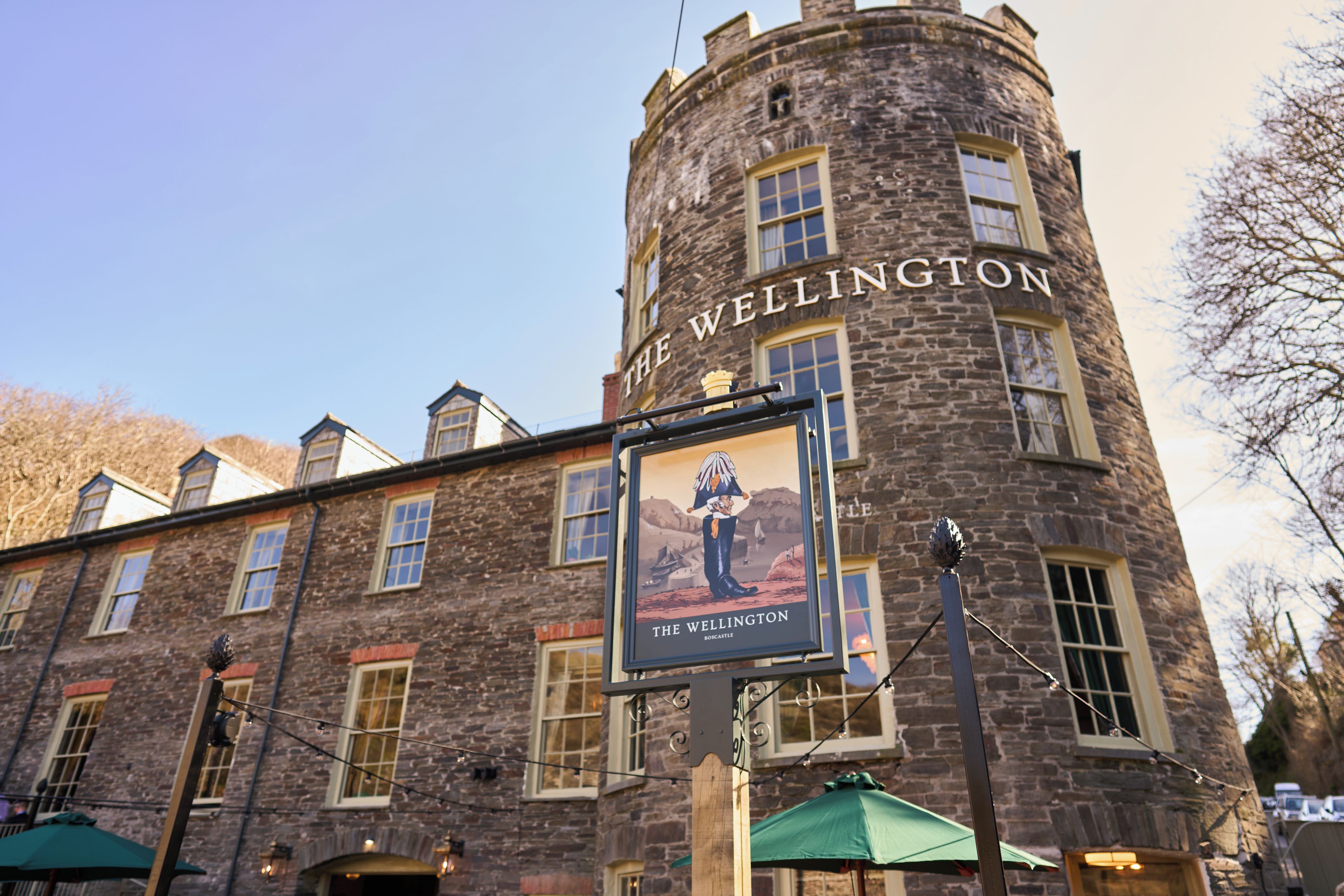 Edifici de pedra històric amb un rètol que diu 'The Wellington' i un cartell d'una persona amb vestimentes tradicionals.