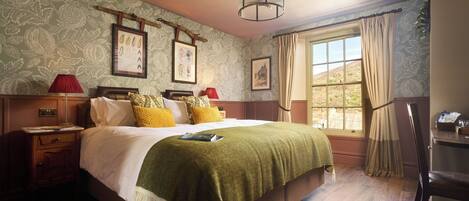 A bedroom with a bed, a nightstand, a lamp, a window with curtains, and a wall-mounted picture.