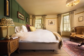A bedroom with a large bed, a wooden nightstand, a lamp, a chair, and a window with curtains. - Wellington Hotel (Boscastle)