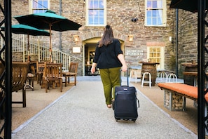 A person walking with a suitcase in a courtyard with stone walls, wooden furniture, and outdoor seating. - Wellington Hotel (Boscastle)