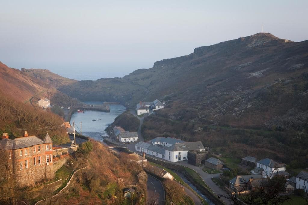A coastal town with a river, stone buildings, and a hill with a wind turbine.