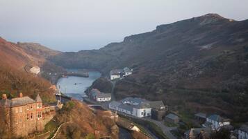 A coastal town with a river, stone buildings, and a hill with a wind turbine.