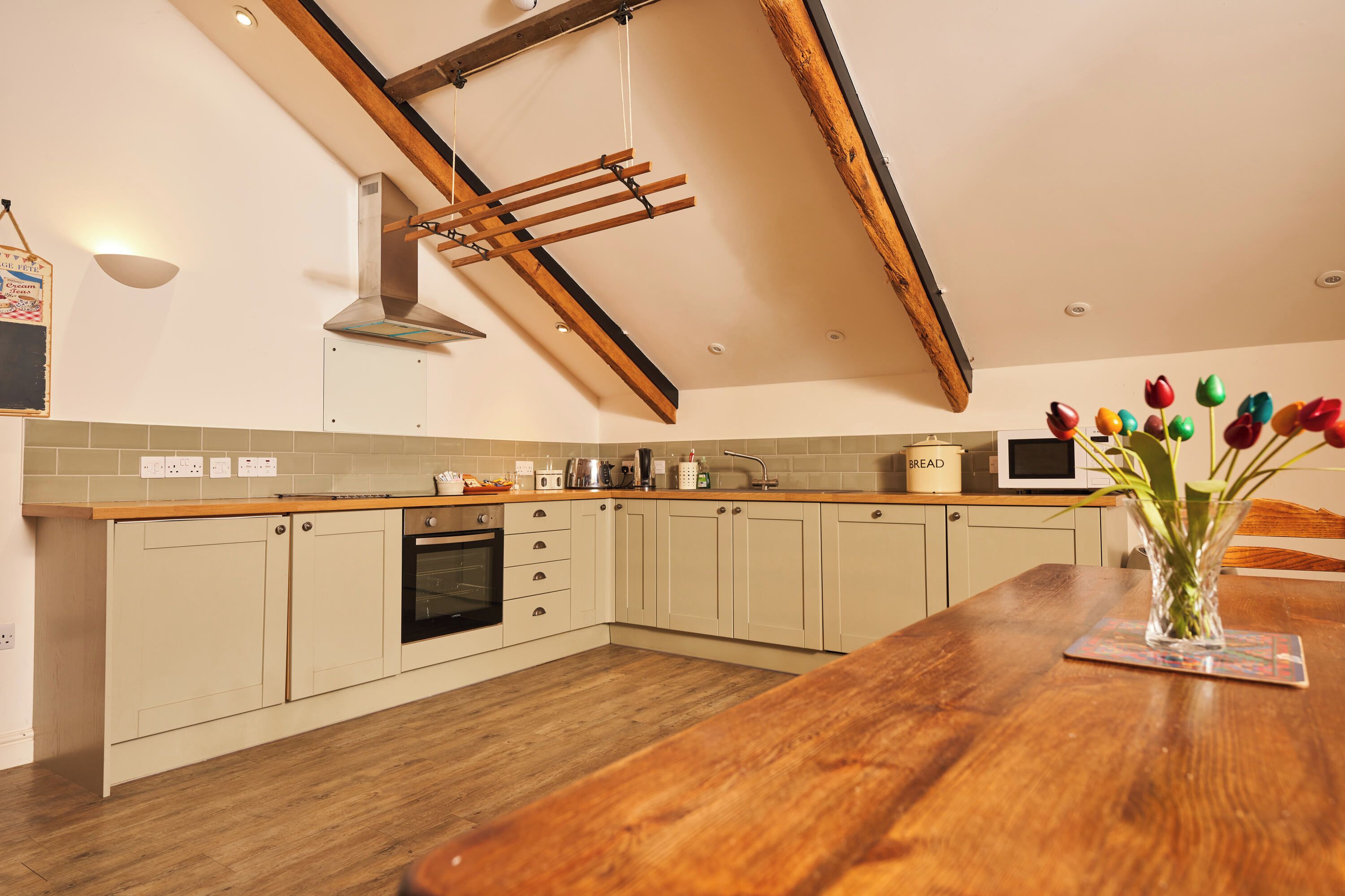 A kitchen with wooden beams, a stove, a microwave, and a vase with flowers on the counter.