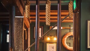 Interior de un restaurante con mesas y sillas de madera, adornos de cuerda colgantes y una pared verde con cuadros enmarcados.