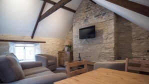 Una habitación acogedora estilo loft con una pared de piedra, un televisor de pantalla plana sobre una mesa de madera y un espacio de estar cómodo con sofás y una silla.