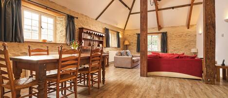 A rustic interior with a wooden dining table, chairs, a sofa, and a bookshelf.