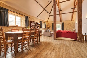 A rustic interior with a wooden dining table, chairs, a sofa, and a bookshelf.