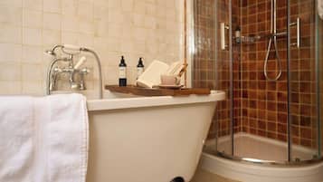 Un baño con bañera, cabina de ducha de cristal y artículos de aseo en el borde de la bañera.