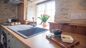 Una cocina con un lavamanos grande, armarios de madera, un ventanal con vistas y un jarrón con flores.