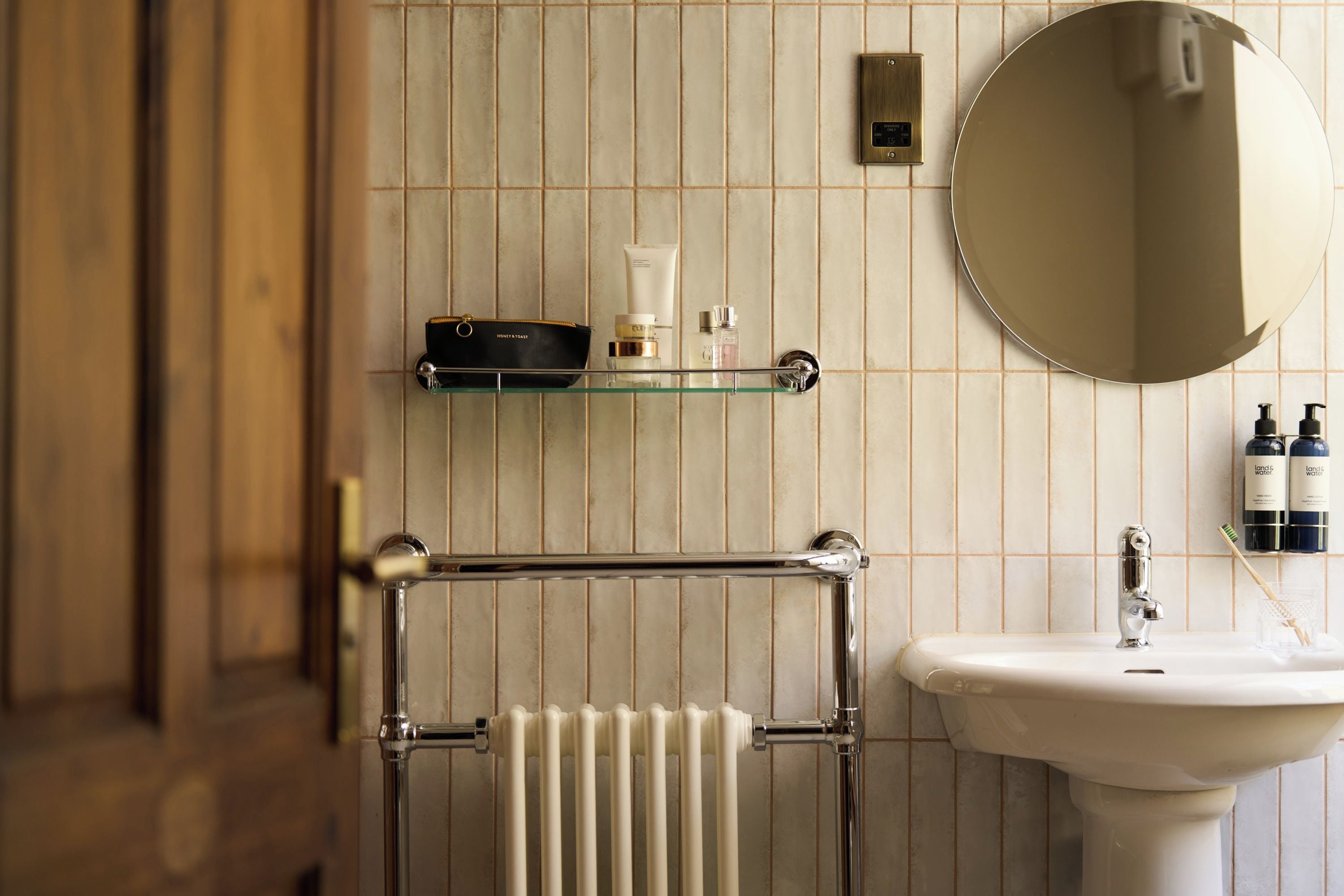 A bathroom with a towel rack, a mirror, a sink, and toiletries on a shelf.