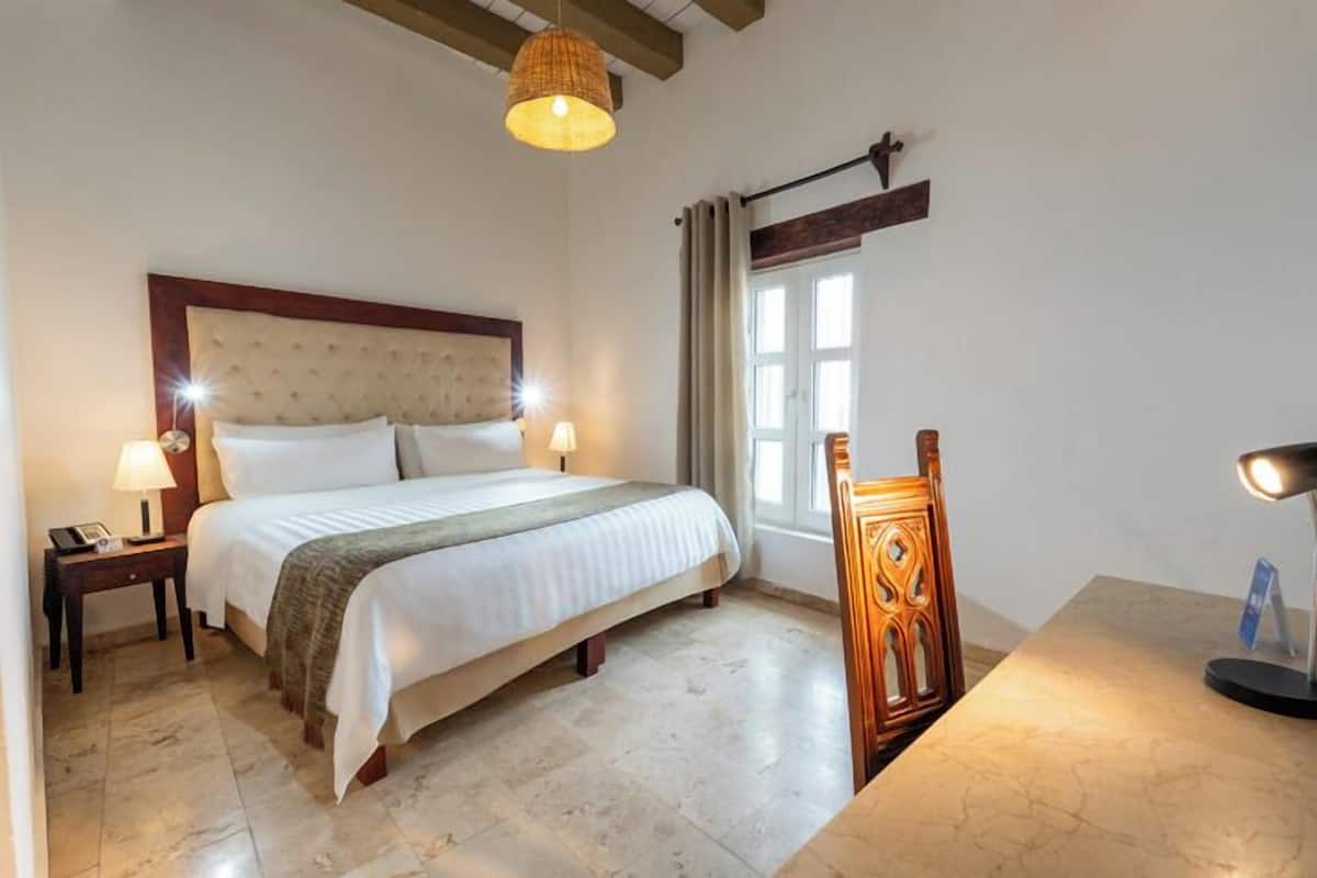 A hotel room with a large bed, two bedside lamps, a wooden chair, and a table with a lamp.