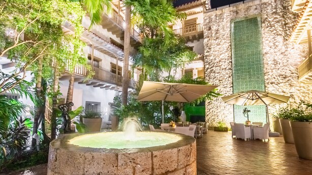 Un cortile con una fontana in pietra, posti a sedere all'aperto e rigogliosa vegetazione.